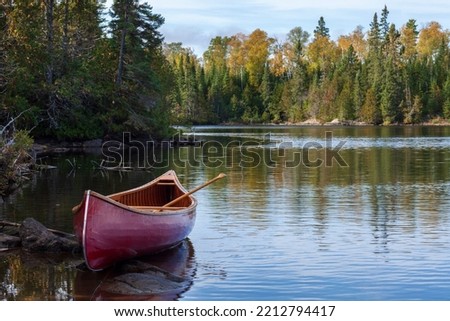Red wooden canoe on the shore of a Boundary Waters lake in morning light during autumn