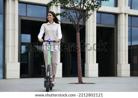 Businesswoman riding electric kick scooter on city street