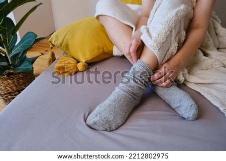 The woman lies in warm gray socks in bed and covers herself with a blanket. Women's legs in cozy socks. View from above. Warm evenings at home Royalty-Free Stock Photo #2212802975
