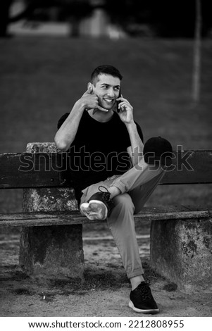 A handsome young man sitting on a bench talking on his cell phone. Black and white photo.