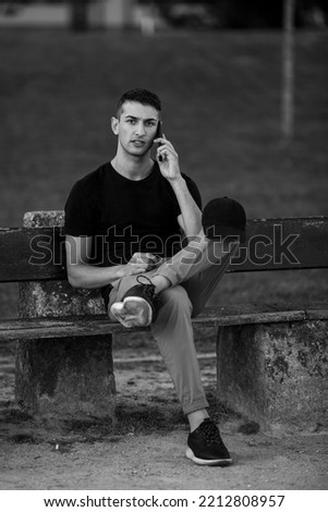 Handsome young man sitting on a bench talking on his phone. Black and white photo.