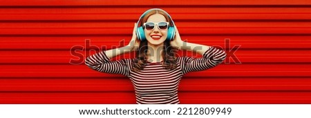 Portrait of happy smiling young woman with headphones listening to music on red background