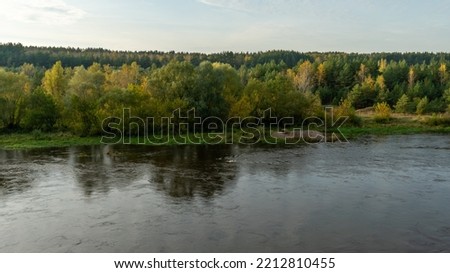 Autumn forest along the river and lake. The setting sun illuminates the treetops. Steep steep sandy bank above a wide river. Autumn walks in ecologically clean places.