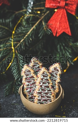 Christmas tree cookies in a craft basket, with selective focus near a blurred Christmas tree with a garland and red bows, close-up side view. Holiday food concept.