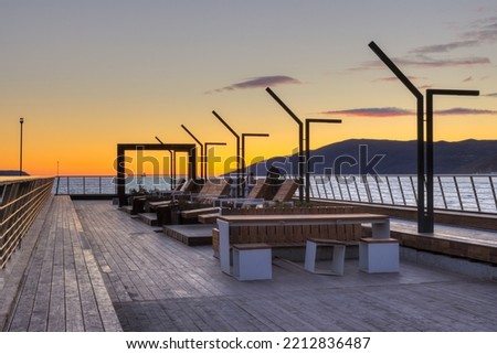 Recreation area on a walking pier in Nagaeva Bay. Beautiful sunset over the Sea of Okhotsk. Development and improvement in Siberia and the Russian Far East. Magadan, Magadan region, Russia. Royalty-Free Stock Photo #2212836487