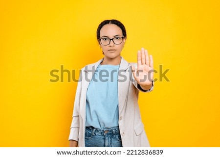 Serious concerned resolute young brunette hispanic or brazilian woman, showing stop gesture with palm, looks at camera, stand on isolated orange background. Against discrimination on women