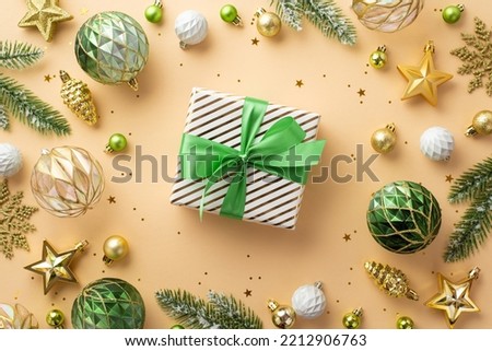 Christmas Eve concept. Top view photo of big gift box with ribbon bow white transparent gold and green baubles snowflake pine cone star ornaments fir branches and confetti on isolated beige background