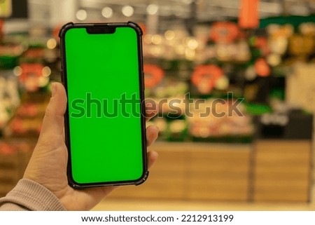 Mobile phone Chroma key for mobile app application. Close up of woman hand holds smart phone with green screen at shopping mall store. Sale Economy Buying food at supermarket, grocery shop center