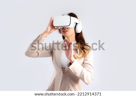 Asian businesswoman in beige color jacket suit wearing vr goggles hand touching on white screen background. Royalty-Free Stock Photo #2212914371
