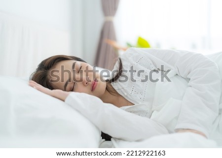 A beautiful woman lays her hands on a soft pillow. A young woman wearing white pajamas lies under a warm blanket. On a comfortable bed in the bedroom enjoy sweet dreams