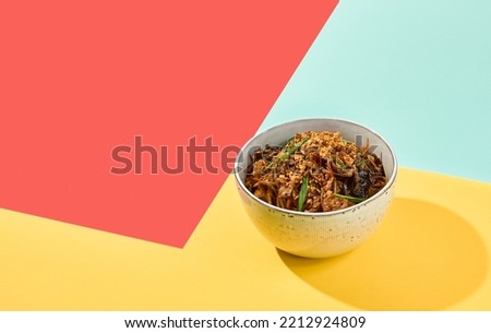 Asian fried buckwheat noodles with chicken on coloured background. Fried noodles in ceramic bowl on yellow, red and blue background. Stir-fry soba in trendy style with shadows. Vibrant food Royalty-Free Stock Photo #2212924809