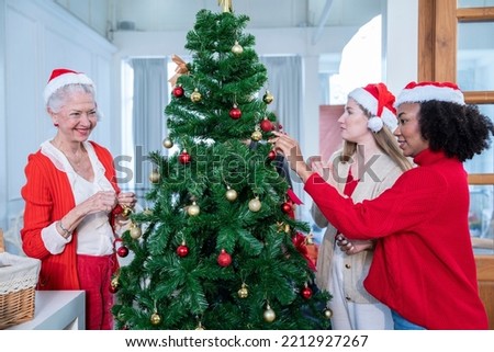 Caucasian grandmother and daughter decorate a Christmas tree with their African American neighbors in their living room during New Year and Christmas.
