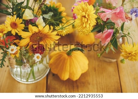 Autumn composition on rustic table. Colorful autumn flowers in vase, pumpkins and pattypan squashes on rustic wooden table. Harvest time in countryside. Hello Fall