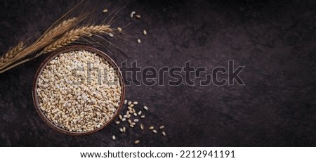 Bowl of dry raw broken pearl barley cereal grain on dark background. Cooking pearl barley porridge concept. Royalty-Free Stock Photo #2212941191