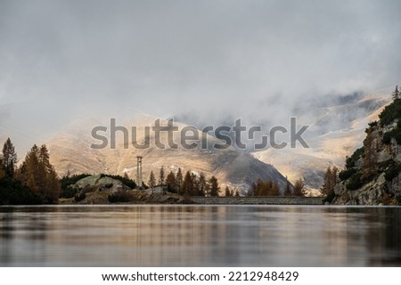 Low angle shot from the surface of the water of Lago Marcio, with orange hills and low clouds in the background, Northern Italy Royalty-Free Stock Photo #2212948429