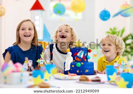 Kids space theme birthday party with cake and cupcakes. Rocket, solar system planet and spaceship decoration for child event. Little boy in astronaut costume blowing candles and opening presents. Royalty-Free Stock Photo #2212949099