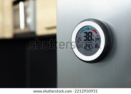 Round digital hygrometer with thermometer on fridge in kitchen. Space for text Royalty-Free Stock Photo #2212950931