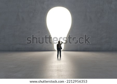 Right decision and idea concept with pensive woman back view looking at the illuminated hole in the form of light bulb on grey wall background