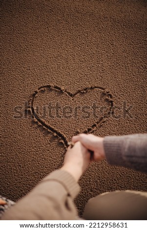 a man and a woman draw a heart in the sand with a stick 