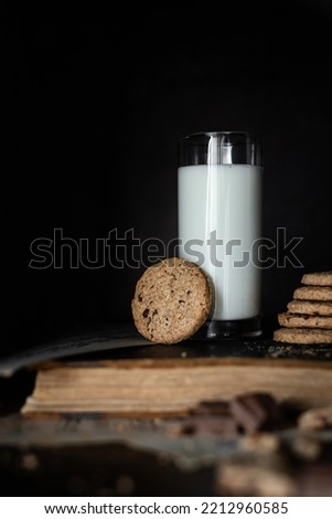 Cookies with and fresh milk placed on an old book. Dark background. Rustic style.