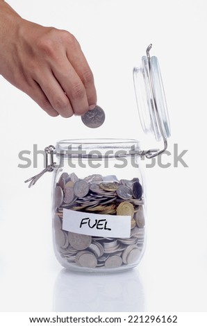 Hand putting a coin into glass jars with 'fuel' text: Saving for fuel consumption