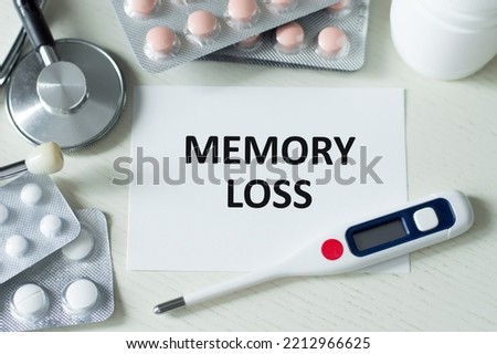MEMORY LOSS written in a card near a stethoscope, pens and pills on a light background. Medical concept