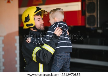 A firefighter take a little child boy to save him. Fire engine car on background. Fireman with kid in his arms. Protection concept