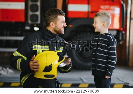 A firefighter take a little child boy to save him. Fire engine car on background. Fireman with kid in his arms. Protection concept Royalty-Free Stock Photo #2212970889