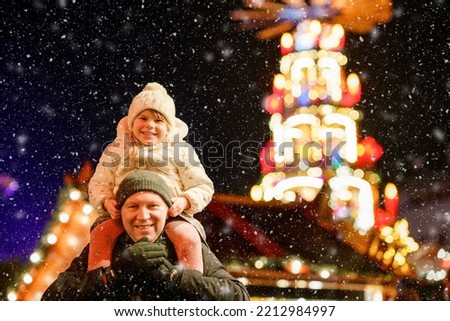 Little preschool girl sitting on shoulder of father on Christmas market in Germany. Happy toddler child and man observing traditional decorated pyramid. Happy family, bonding, love. Family xmas time.