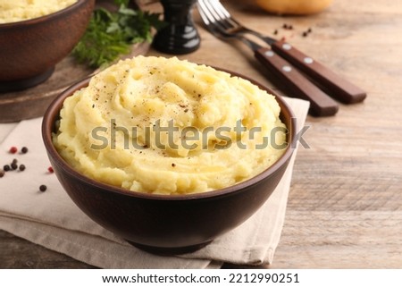 Bowl of tasty mashed potatoes with black pepper served on wooden table Royalty-Free Stock Photo #2212990251