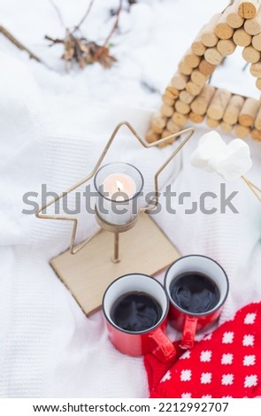 Christmas background, red mittens, cups of coffee on the snow, star candle. Selective focus, noise. Outdoor picnic. Merry Christmas