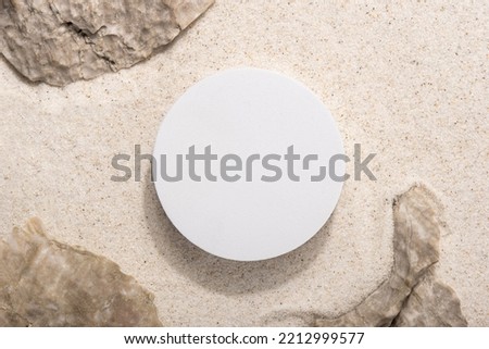 Natural cosmetic background for product presentation. Rocks and white podium on the sand. Top view.