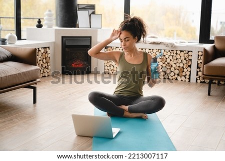 Tired exhausted african young fit healthy woman athlete in sporty clothes relaxing after yoga workout training, physical exercises on fitness mat, watching online video tutorial on laptop at home Royalty-Free Stock Photo #2213007117