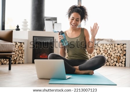 Online vlogging blogging training on fitness mat on laptop. African young female athlete doing yoga exercises at home, having videocall, video tutorial Royalty-Free Stock Photo #2213007123