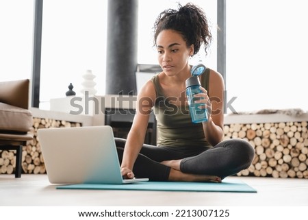 Closeup online vlogging blogging training on fitness mat on laptop. African young female athlete doing yoga exercises at home, having videocall, video tutorial Royalty-Free Stock Photo #2213007125