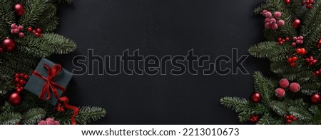 Christmas winter banner with gift, fir branches, red balls on black background. Xmas greeting card. Holiday time. Happy New Year. Space for text. View from above, flat lay.