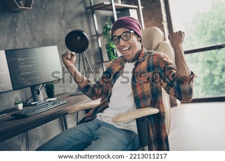 Photo of cheerful successful freelancer wear hat glasses celebrating great job offer indoors workplace workstation loft