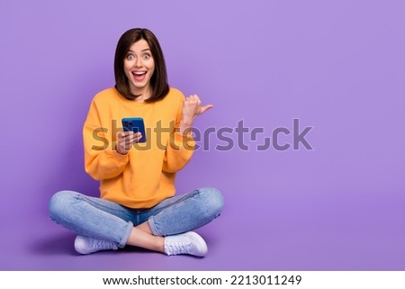 Full body size photo of young woman blogger influencer hold smartphone sitting finger point empty space eshopping promo isolated on violet color background