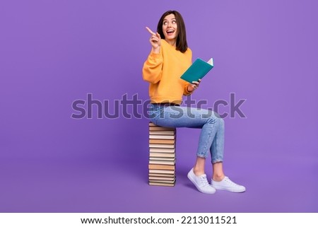 Full body size photo of charming attractive girl wear orange shirt reading new book literature finger point empty space isolated on violet color background