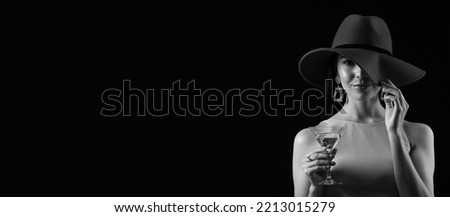 Black and white portrait of beautiful young woman drinking martini on dark background with space for text