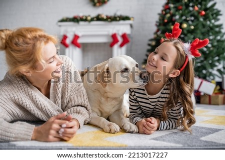 Smiling mother looking at daughter with christmas headband and labrador at home