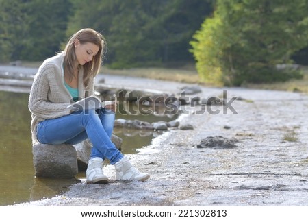 Girl relaxing reading book, near lake