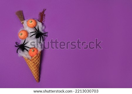 Halloween icecream made with ice-cream cone, spider web, witch's broom and pumpkins on purple background. Halloween sweet dessert. Flat lay, copy space