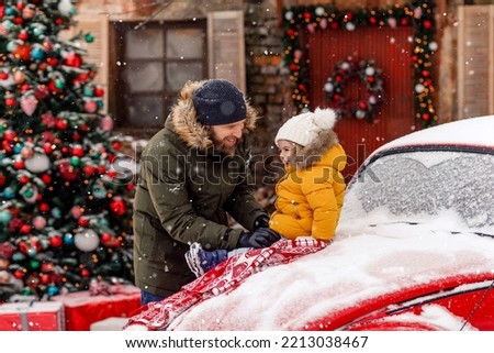 Father and child play outside in snow winter time near red vintage car. Christmas and New Year tree cozy background. Concept of family and happiness. Snowflakes and colorful winter outerwear