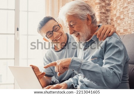 Smiling young boy helping senior grandfather with laptop choose goods or services via internet or web surfing together at home. Younger generation caring about older relatives teaching using computer Royalty-Free Stock Photo #2213041605