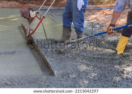 In construction new driveway, machine is used to align on compacted layer fresh concrete Royalty-Free Stock Photo #2213042297