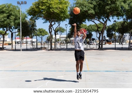 Young muslim man playing street basketball in a city court, throwing ball, training and sport concept