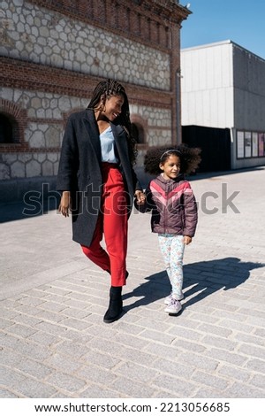Cute afro young girl holding her mother’s hand and smiling in the street.