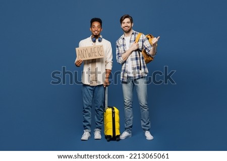Full body two friend men wear shirt hold bag card sign anywhere do hitch-hiking gesture isolated on plain dark blue background. Tourist travel abroad in free time rest getaway. Air flight trip concept