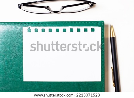On a light background, glasses, a pen, a green notepad and a white blank sheet of paper with a place to insert text